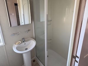 Un baño con lavamanos blanco, un espejo y cabina de ducha de vidrio.