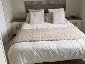 A neatly made bed with a beige and white color scheme, a woven throw blanket, and a headboard with a textured pattern. - Trecco Bay Holiday Park, Porthcawl (Porthcawl)
