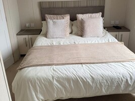 A neatly made bed with a beige and white color scheme, a woven throw blanket, and a headboard with a textured pattern.