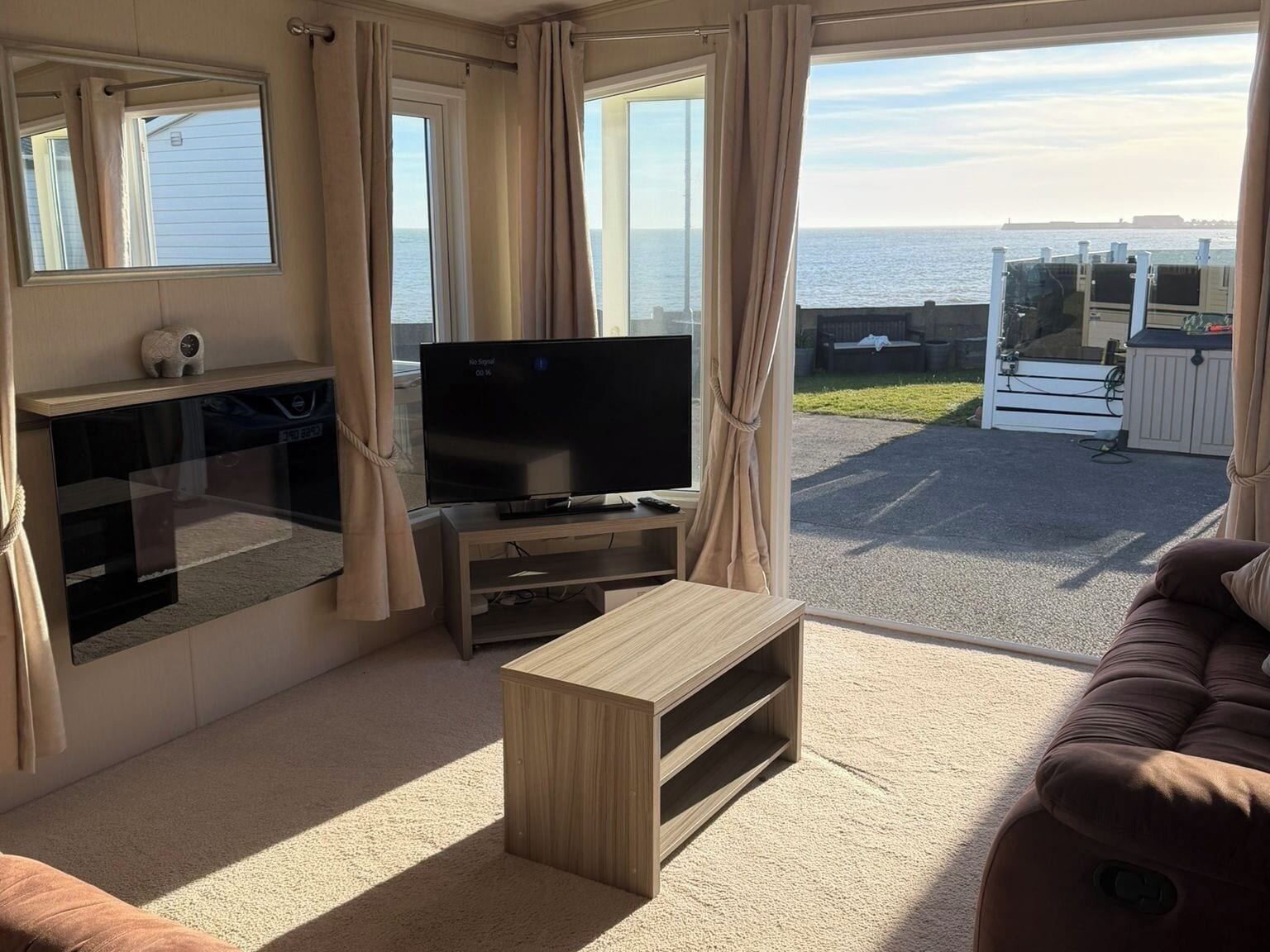 Uma sala de estar com televisão, mesa de centro de madeira, sofá e vista para o mar.