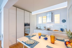 Una cucina moderna con elettrodomestici integrati, un tavolo da pranzo apparecchiato con piatti e bicchieri, e una ciotola di frutta sul piano di lavoro.