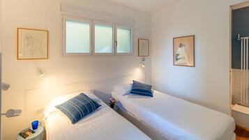 Una camera d'albergo con due letti, una finestra con vetro satinato, un'opera d'arte appesa al muro, un comodino con una lampada e un termosifone.
