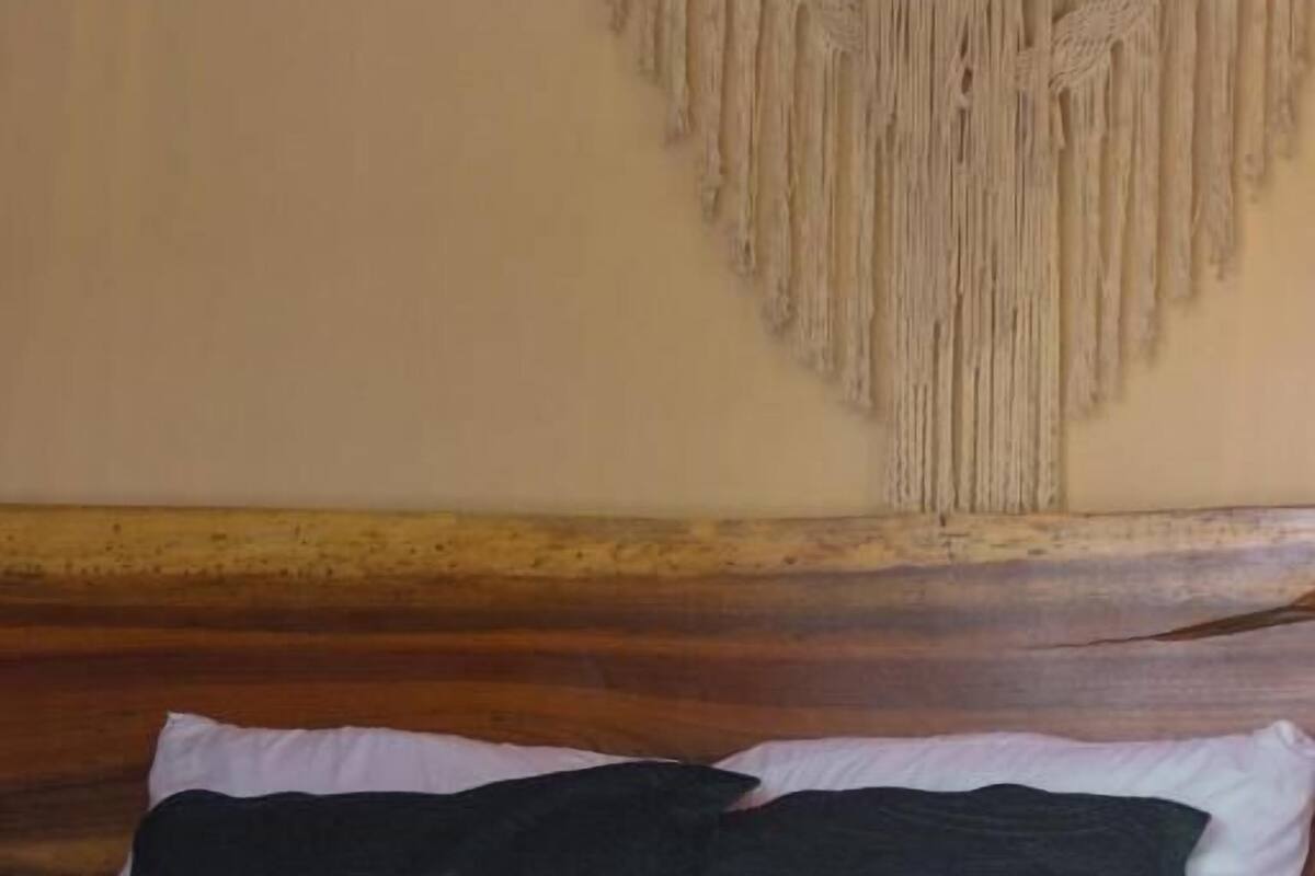 Una cama con estructura de madera, una colcha verde y dos almohadas.
