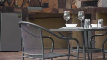Un área de comedor al aire libre con sillas de metal y una mesa, suelo de piedra y una cocina al fondo.