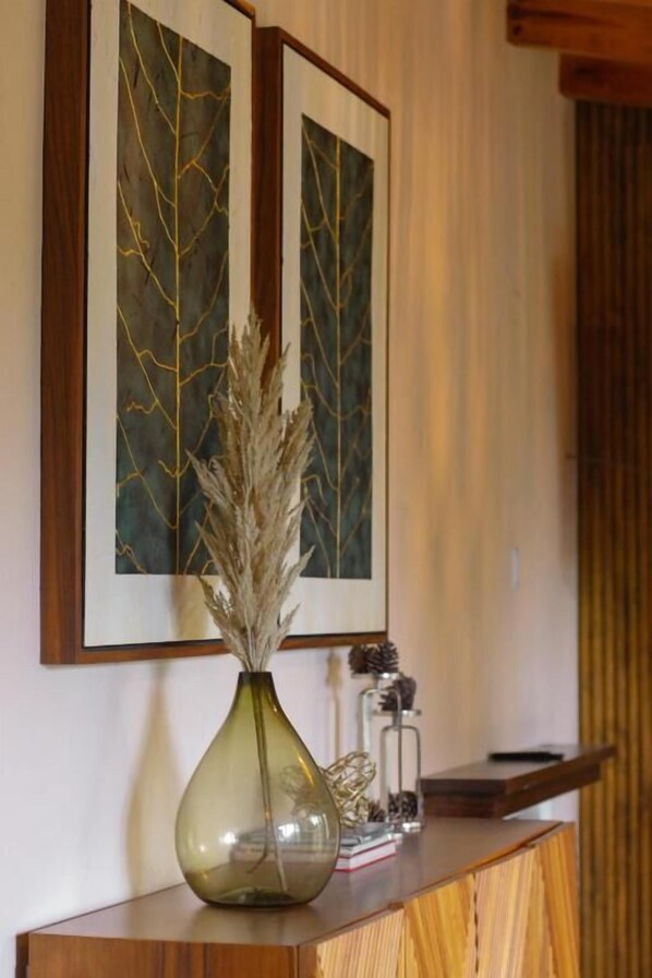 Una consola de madera con un florero de plantas secas, una obra de arte enmarcada y objetos decorativos.