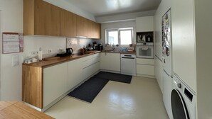 Une cuisine moderne avec des meubles en bois, un four encastré, un lave-linge et une fenêtre qui laisse entrer la lumière naturelle.