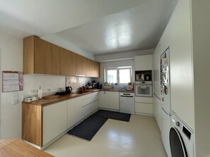 A modern kitchen with wooden cabinets, a built-in oven, a washing machine, and a window providing natural light. - The Blue House Estoril, Pergola and Lounge - 5 mins from the beachand woodland (Estoril)