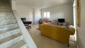 Un salon comprenant un canapé, un téléviseur, une bibliothèque, un globe terrestre et un escalier.