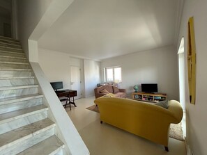 A living room with a sofa, a television, a bookshelf, a globe, and a staircase. - The Blue House Estoril, Pergola and Lounge - 5 mins from the beachand woodland (Estoril)
