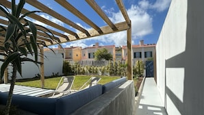 Un espace extérieur abrité, doté d’un banc en béton, d’une pergola en bois et offrant une vue sur des immeubles d’habitation en arrière-plan.