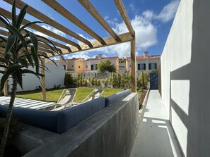 A covered outdoor area with a concrete bench, a wooden pergola, and a view of residential buildings in the background. - The Blue House Estoril, Pergola and Lounge - 5 mins from the beachand woodland (Estoril)
