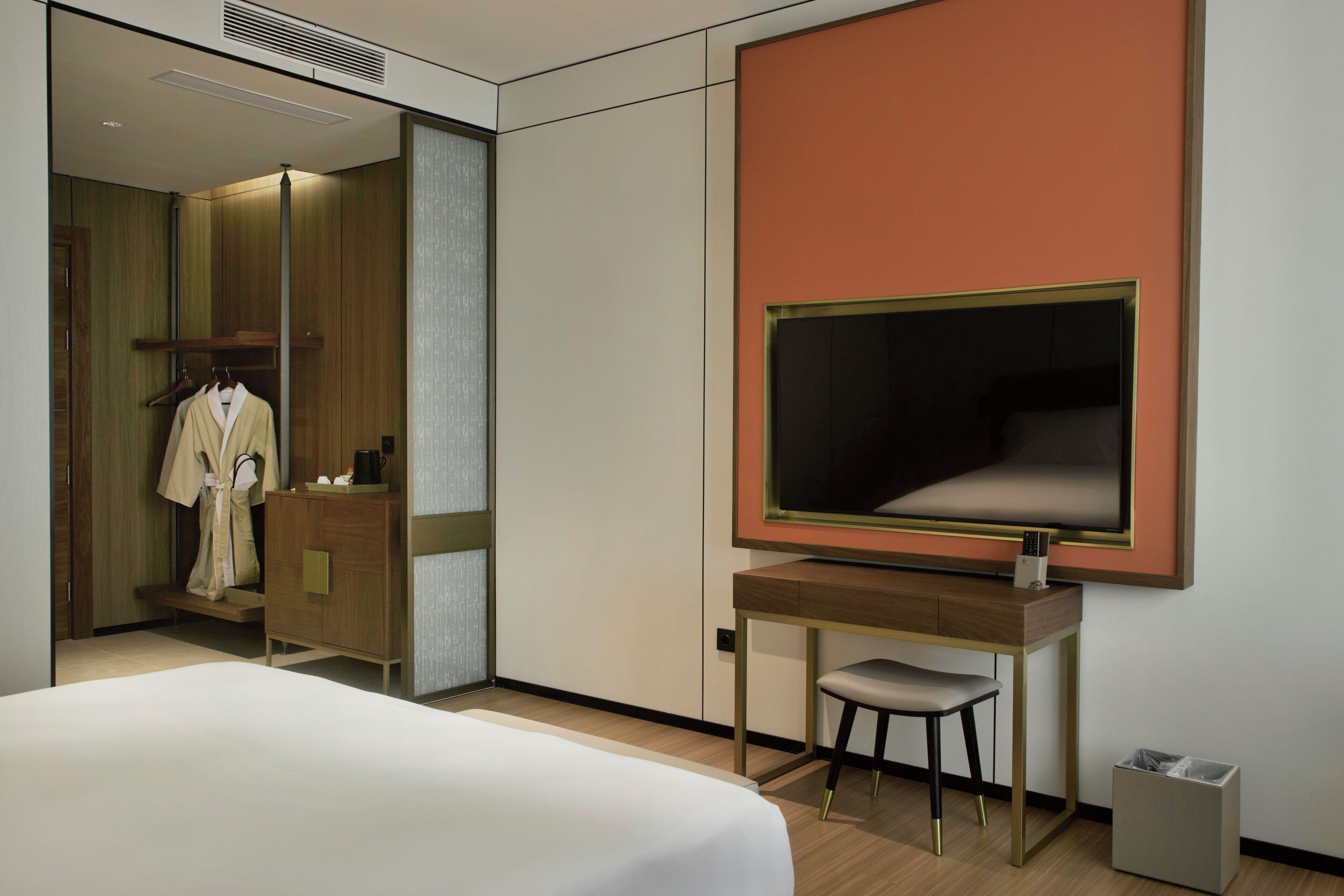 A hotel room with a bed, a desk, a chair, a wardrobe, and a large mirror.