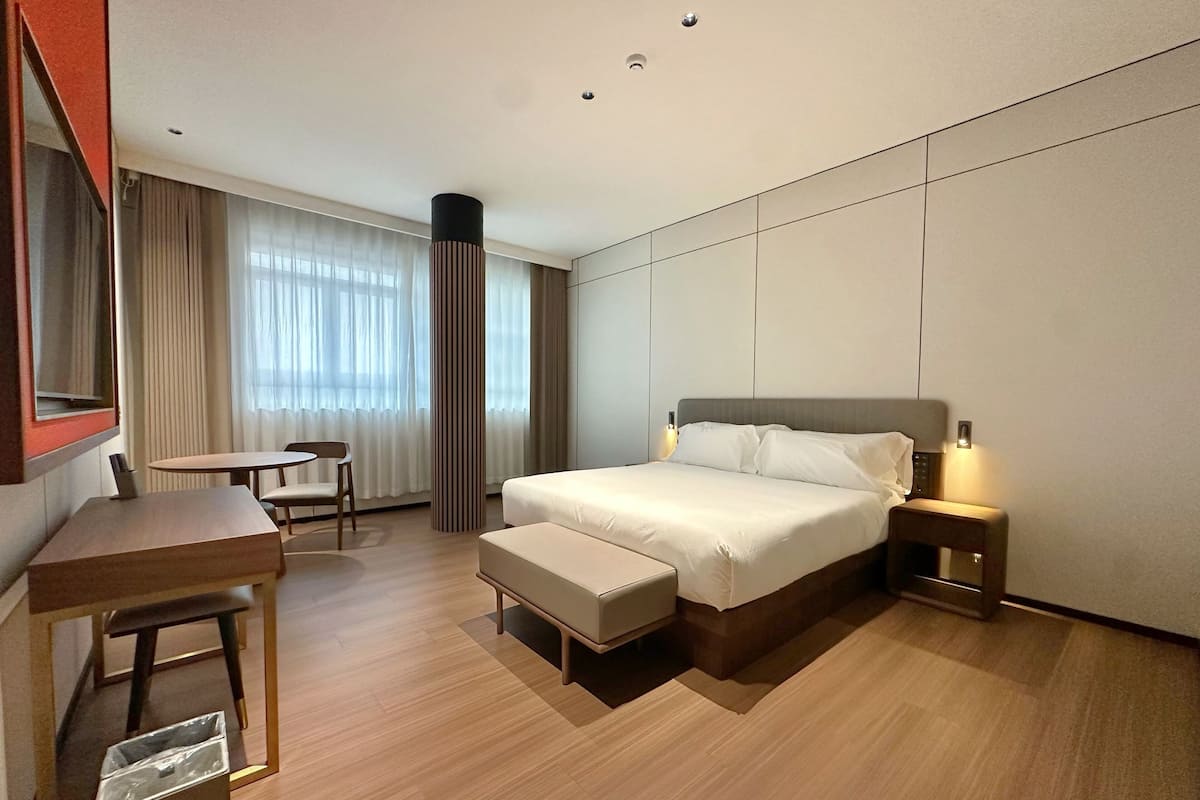 Una habitación de hotel con cama, mesita de noche, silla, escritorio y un espejo grande.