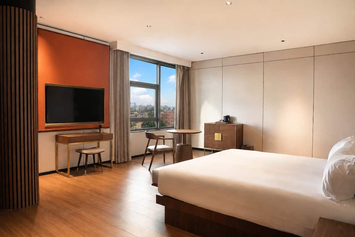 Habitación de hotel con cama, escritorio con silla, televisor, una mesita y un armario.