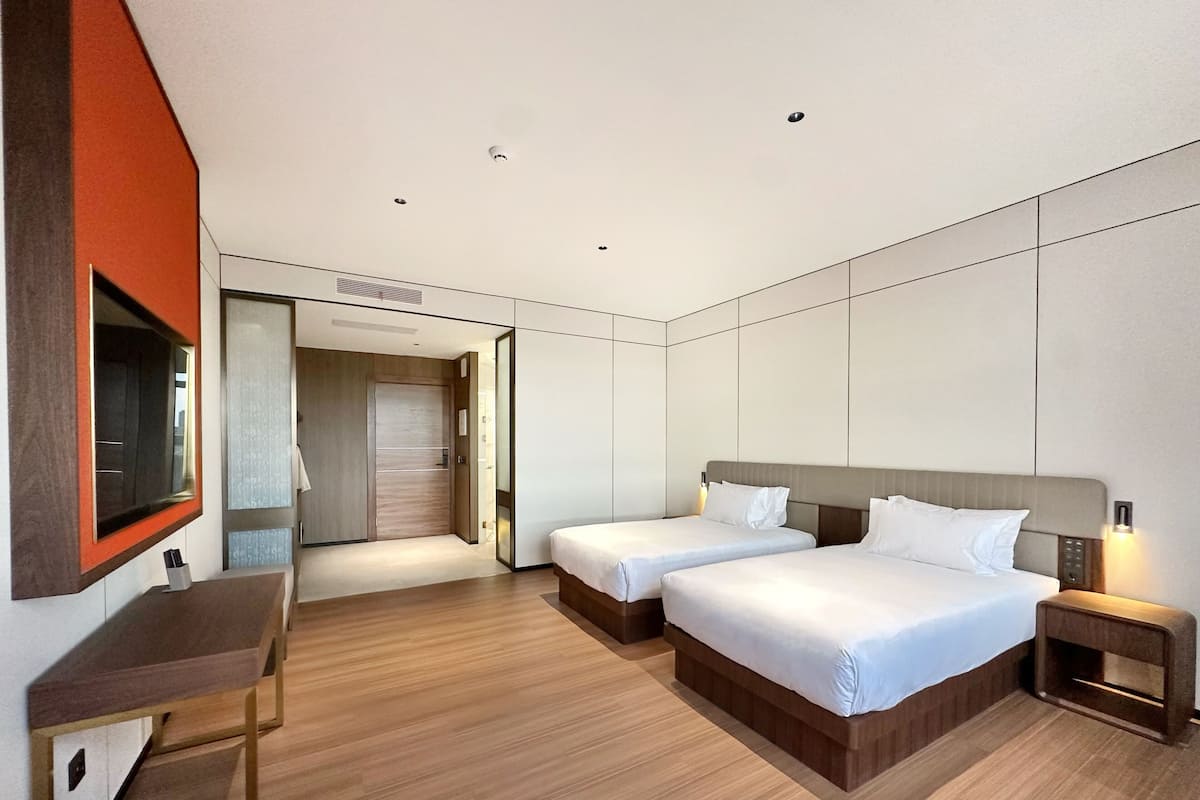 Habitación de hotel moderna con dos camas, un escritorio y un espejo.