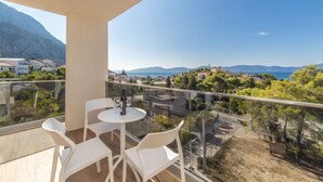 A balcony with a table and chairs, overlooking a coastal landscape with buildings and mountains. - Altiora Prestige Residence 301 (Gradac)