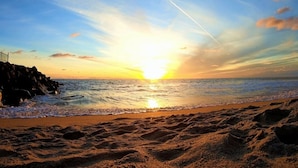 Ein Strand bei Sonnenuntergang, mit Wellen und einer Kondensstrecke.