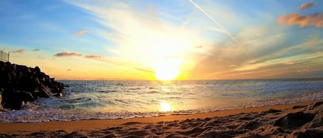 A beach with a sunset, waves, and a jet trail.