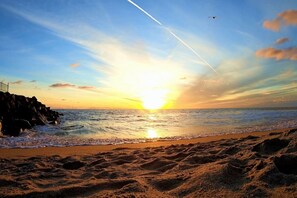 Ein Strand bei Sonnenuntergang, mit Wellen und einer Kondensstrecke.