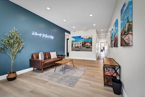 Eine moderne Lobby mit blauer Akzentwand, einem Ledersofa, einem Holztisch und einem Empfangstresen mit gerahmten Kunstwerken.