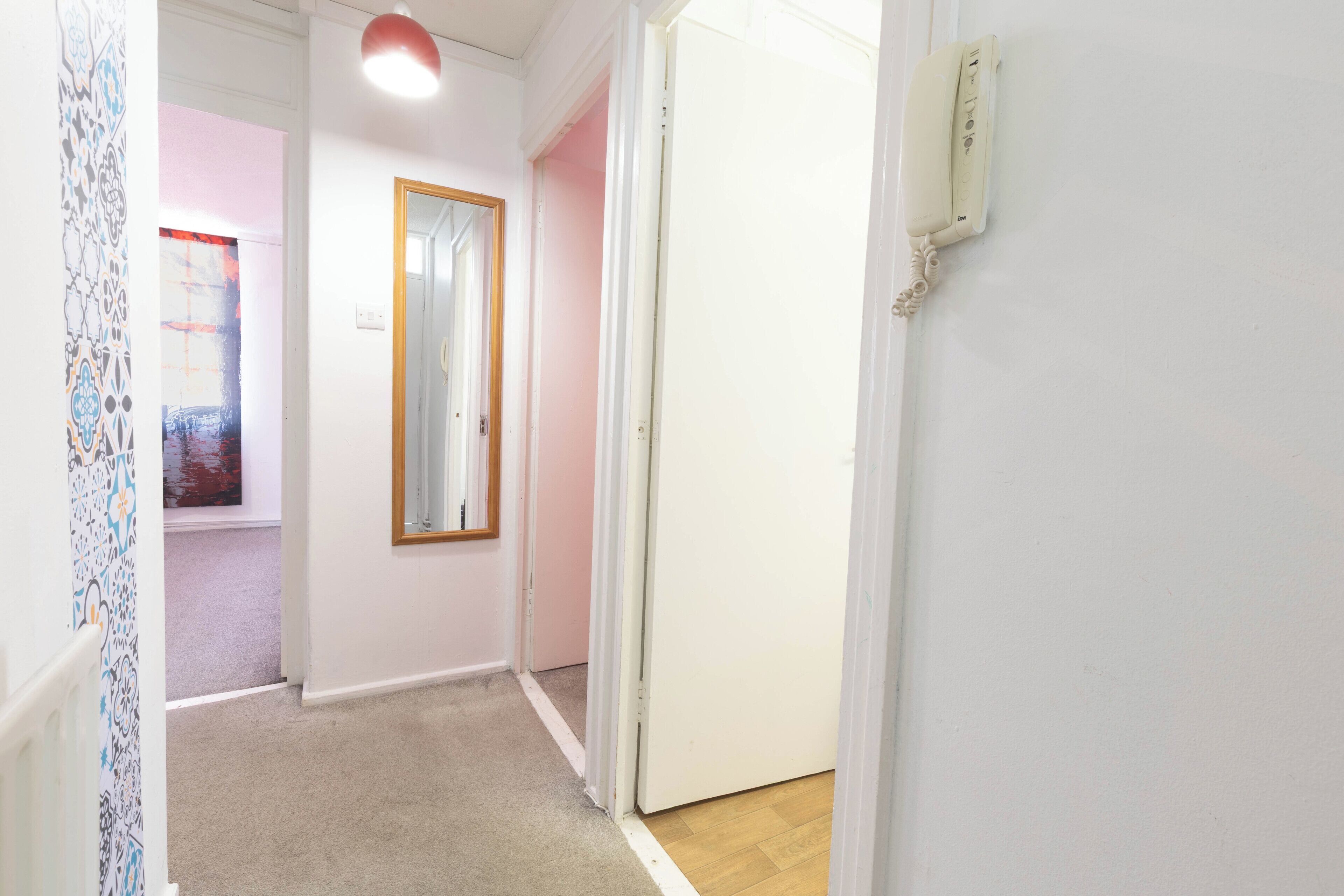 Un couloir doté d’un sol recouvert de moquette, d’une porte avec un interrupteur et d’un mur orné d’un motif décoratif.