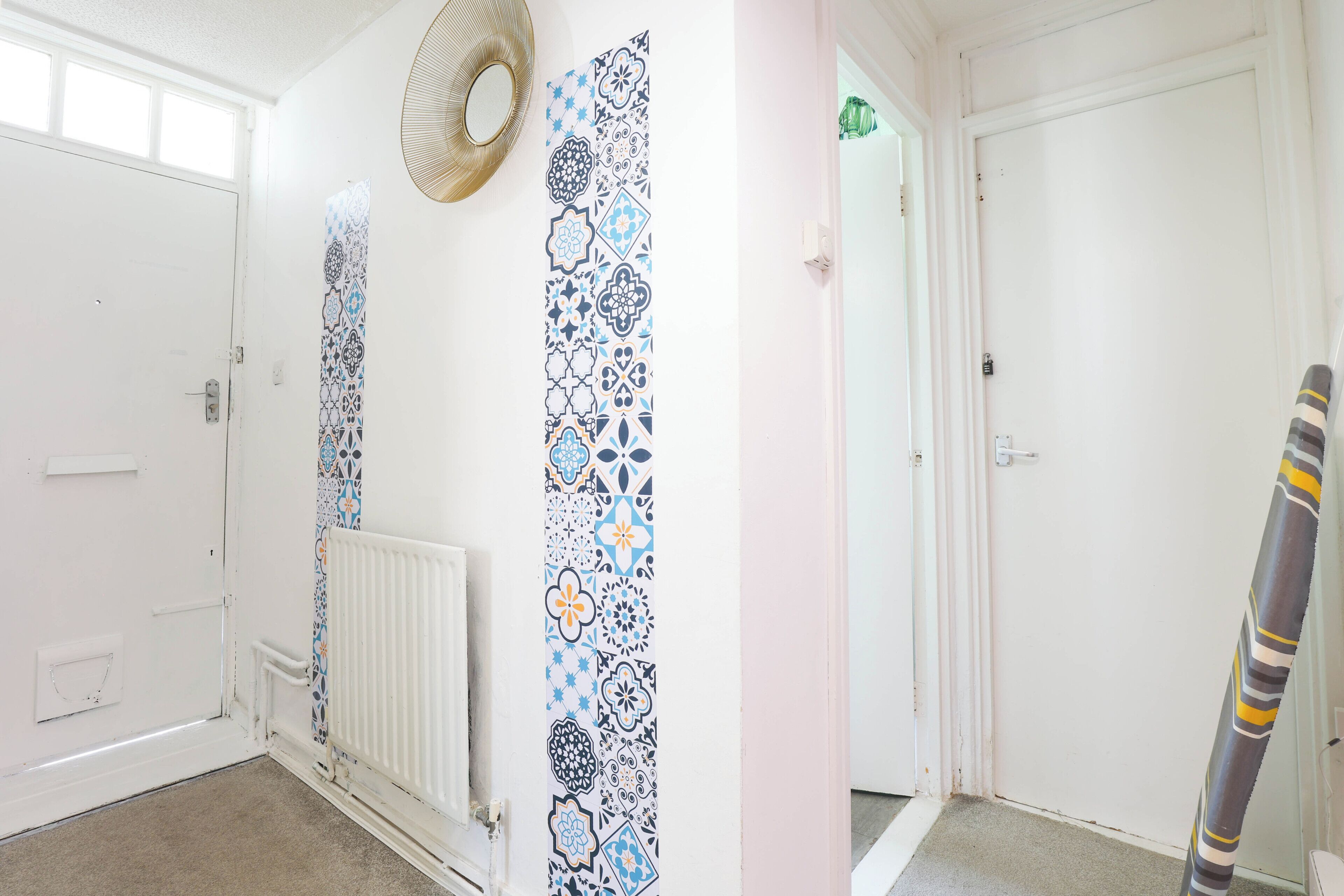 A hallway with patterned wallpaper, a radiator, a door, and a striped object leaning against the wall.