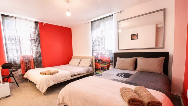 Ein Hotelzimmer mit zwei Betten, einer roten Akzentwand, einem großen Spiegel und Blick auf einen roten Doppeldeckerbus.