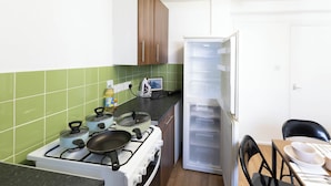 Eine Küche mit Herd, Töpfen, einem Kühlschrank und einem Esstisch mit Stühlen.