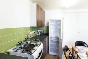 A kitchen with a stove, pots, a refrigerator, and a dining table with chairs. - 3BR Flat in King`s Cross, St. Pancras Area - 10 minutes walk to tube (London)