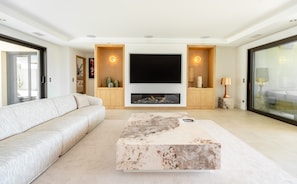 A modern living room with a large flat-screen TV, a fireplace, a sofa, and a coffee table. - Superb villa with swimming pool in a secure estate close to the beach and town center (Sainte-Maxime)