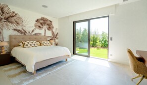 A bedroom with a bed, a nightstand, a lamp, a chair, and a sliding glass door leading to a garden. - Superb villa with swimming pool in a secure estate close to the beach and town center (Sainte-Maxime)