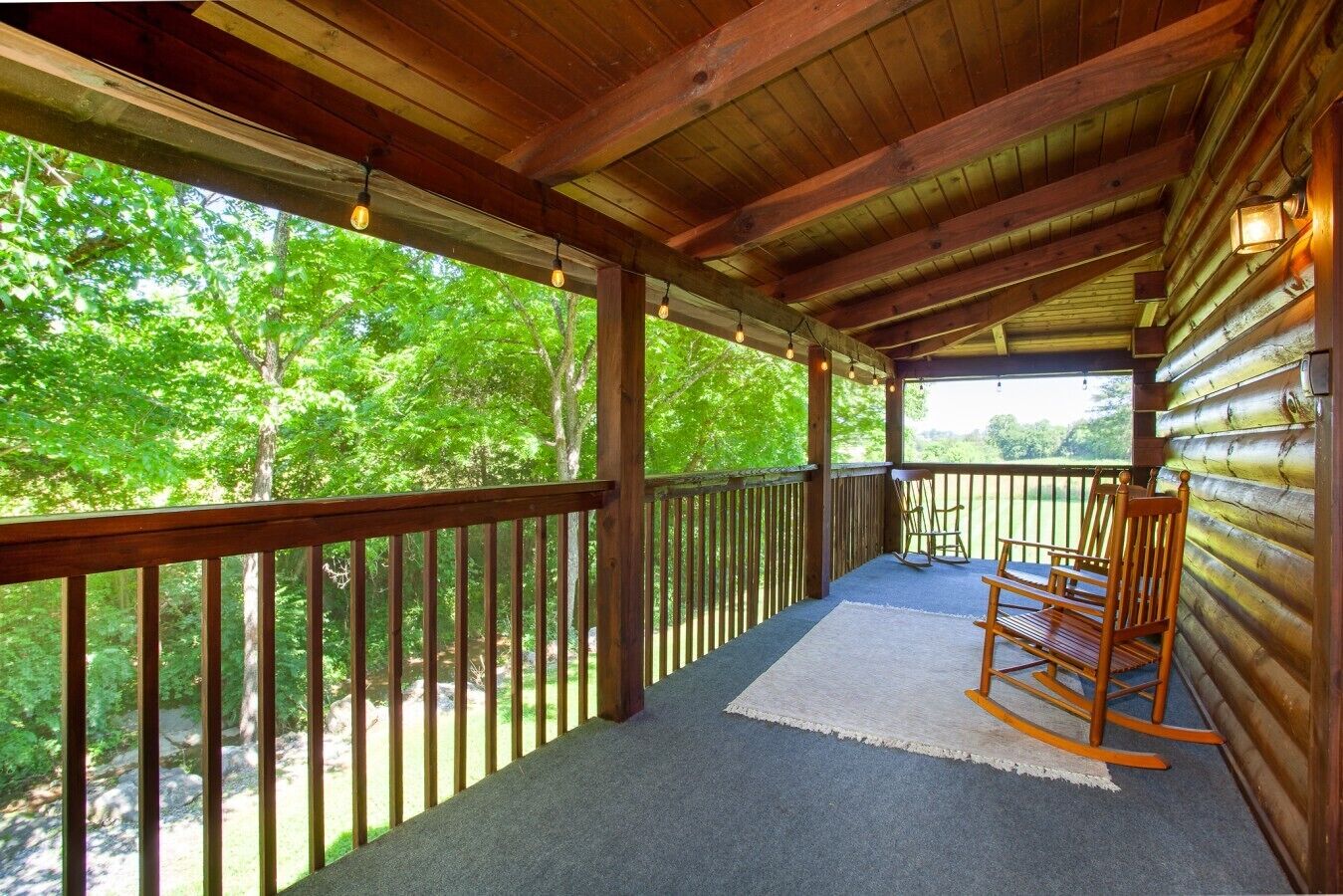 A wooden deck with a rocking chair, a rug, and a railing overlooking a forested area.