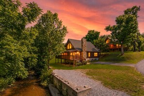 A lodge with a stone chimney, wooden exterior, and a porch with outdoor seating. - Creekfront Pet Friendly & Perfect for the Family! (Sevierville)