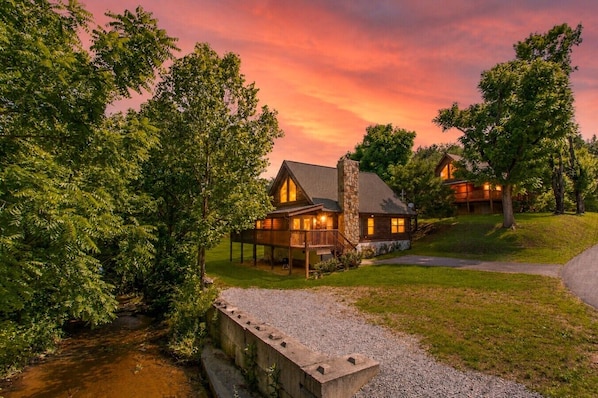 Eine Lodge mit Kamin aus Stein, Holzfassade und einer Veranda mit Sitzgelegenheit im Freien.