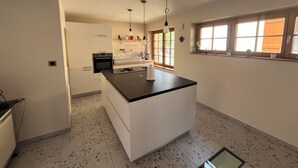 A modern kitchen with a central island, white cabinetry, and a window with a view. - Gîte de la Rivière, 3 stars, sleeps 2 to 6, Munster, Colmar, wine routes, and mountain ridges (Breitenbach-Haut-Rhin)