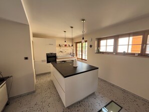 A modern kitchen with a central island, white cabinetry, and a window with a view. - Gîte de la Rivière, 3 stars, sleeps 2 to 6, Munster, Colmar, wine routes, and mountain ridges (Breitenbach-Haut-Rhin)