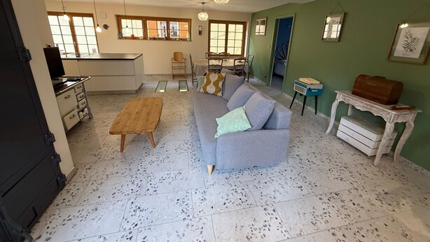 A living room with a grey sofa, wooden coffee table, and a kitchen area with a white countertop. - Gîte de la Rivière, 3 stars, sleeps 2 to 6, Munster, Colmar, wine routes, and mountain ridges (Breitenbach-Haut-Rhin)