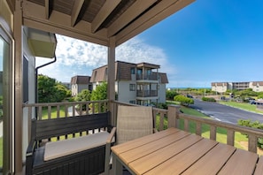 A balcony with a wooden table and bench, overlooking a residential area with houses and a road. - Southwinds Hideaway| Pool · Private Beach · 2BR AB (Atlantic Beach)