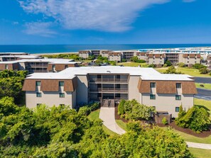 A multi-story hotel with a flat roof, surrounded by greenery and a clear view of the ocean. - Southwinds Hideaway| Pool · Private Beach · 2BR AB (Atlantic Beach)