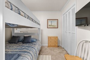 A bedroom with bunk beds, a wooden dresser, a framed picture on the wall, and a closet with white shutters. - Southwinds Hideaway| Pool · Private Beach · 2BR AB (Atlantic Beach)
