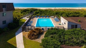 Una piscina con vista a la playa, rodeada de vegetación y un edificio.