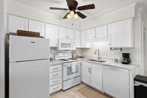 Eine Küche mit weißen Schränken, einem Kühlschrank, einer Mikrowelle, einem Backofen, einem Spülbecken und einem Deckenventilator.