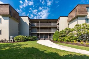A multi-story residential building with a central courtyard, balconies, and a well-maintained lawn. - Southwinds Hideaway| Pool · Private Beach · 2BR AB (Atlantic Beach)