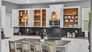 A modern kitchen with white cabinets, a central island, pendant lighting, and a dining area with chairs. - Commercial Mario Arcade • Star Wars & Candy Rooms • 10 Mi Disney (Kissimmee)