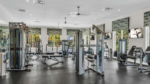 A gym with various exercise machines, a ceiling fan, and large windows with a view of palm trees. - Commercial Mario Arcade • Star Wars & Candy Rooms • 10 Mi Disney (Kissimmee)