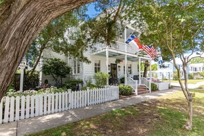 Ein weißes, zweistöckiges Haus mit Veranda und weißem Zaun, geschmückt mit amerikanischen Flaggen.