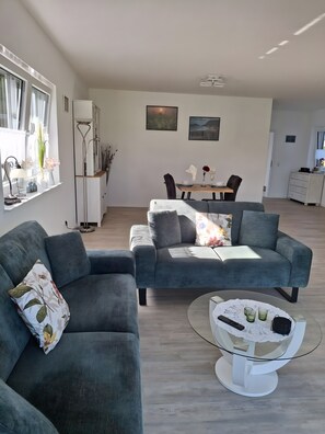 A modern living room with two grey sofas, a dining table with chairs, and a kitchen area in the background. - Apartment 'Kleine Schwalbe' with Private Terrace and Wi-Fi (Rechtsupweg)