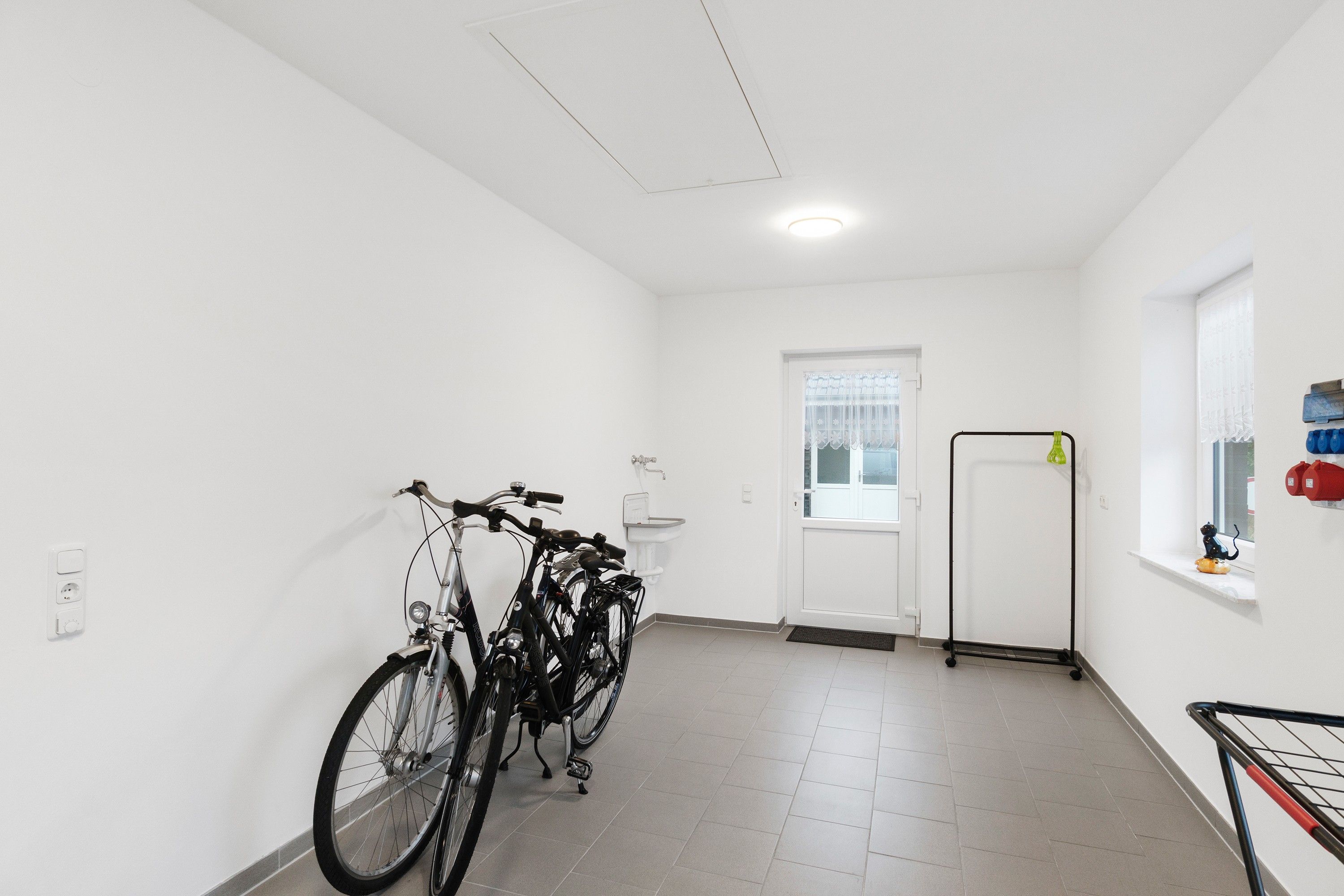 Ein sauberer, gut beleuchteter Flur mit Fahrrädern an der Wand, einer Tür und einem Fenster mit Aussicht.