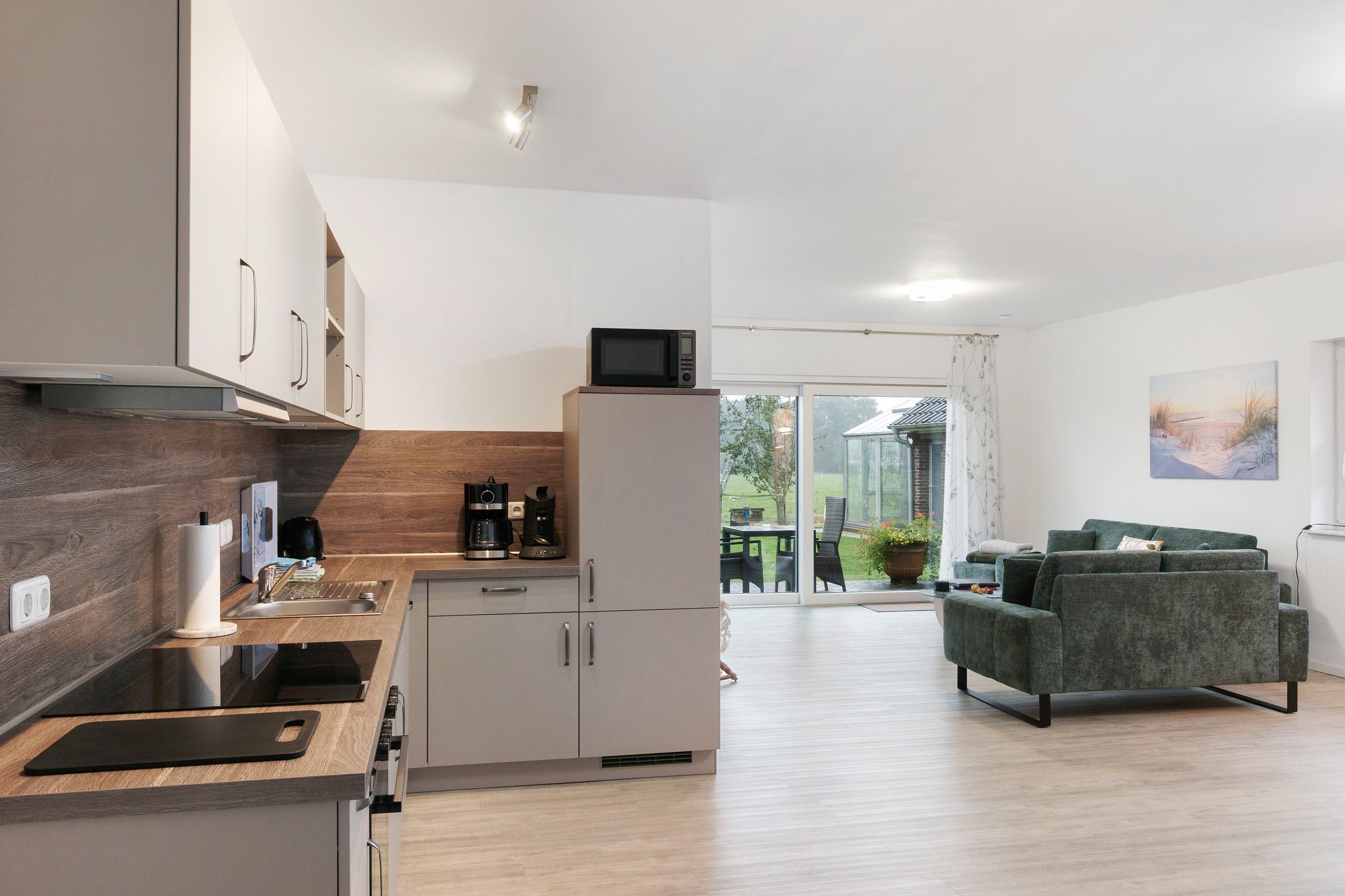 Eine moderne Küche mit integriertem Mikrowellenherd, einer Kaffeemaschine und einem Spülbecken. Es gibt einen Essbereich mit Tisch und Stühlen, und ein grünes Sofa im Wohnzimmer.
