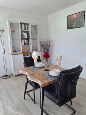 Ein Essbereich mit einem Holztisch, schwarzen Stühlen, einem weißen Bücherregal und einem gerahmten Bild an der Wand.